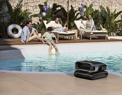 Robot limpiapiscinas Beatbot sobre el borde de una piscina exterior mientras una familia disfruta del sol en tumbonas al fondo