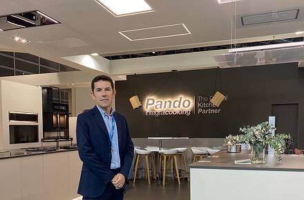 Sergio Seña, nuevo director general de Pando Integral Cooking, posando en traje azul marino en el showroom de la compañía con el logo iluminado al fondo