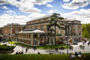 Vista exterior del Museo Nacional del Prado en Madrid con visitantes paseando por los jardines y cartel de la exposición Georges de La Tour en fachada
